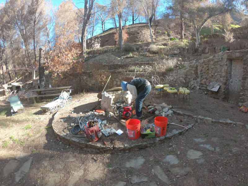 Person working at a fire pit by the well with burned hillside behind
