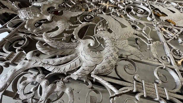 Close-up of pale gray wrought iron bird figures with feather detail, surrounded by scrollwork, lying on a shop floor.