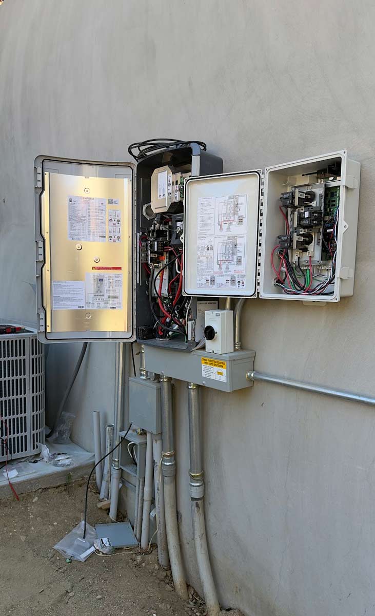Open Enphase electrical enclosures mounted on a stucco wall, showing wiring, breakers and a rapid-shutdown label, with conduit running below.