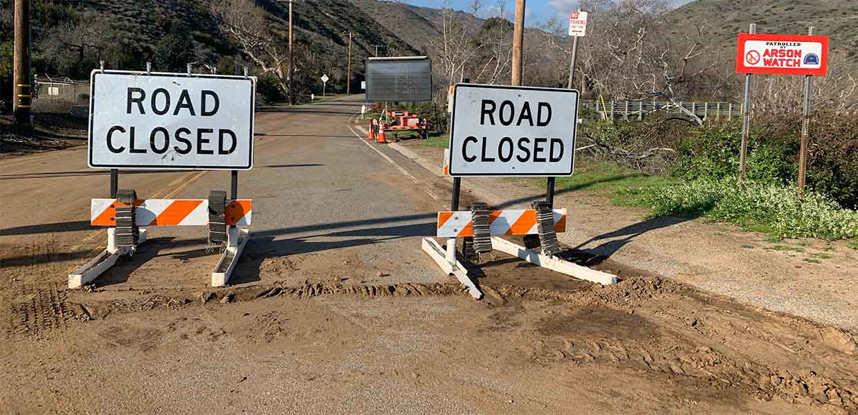 Two ROAD CLOSED signs on a muddy canyon road