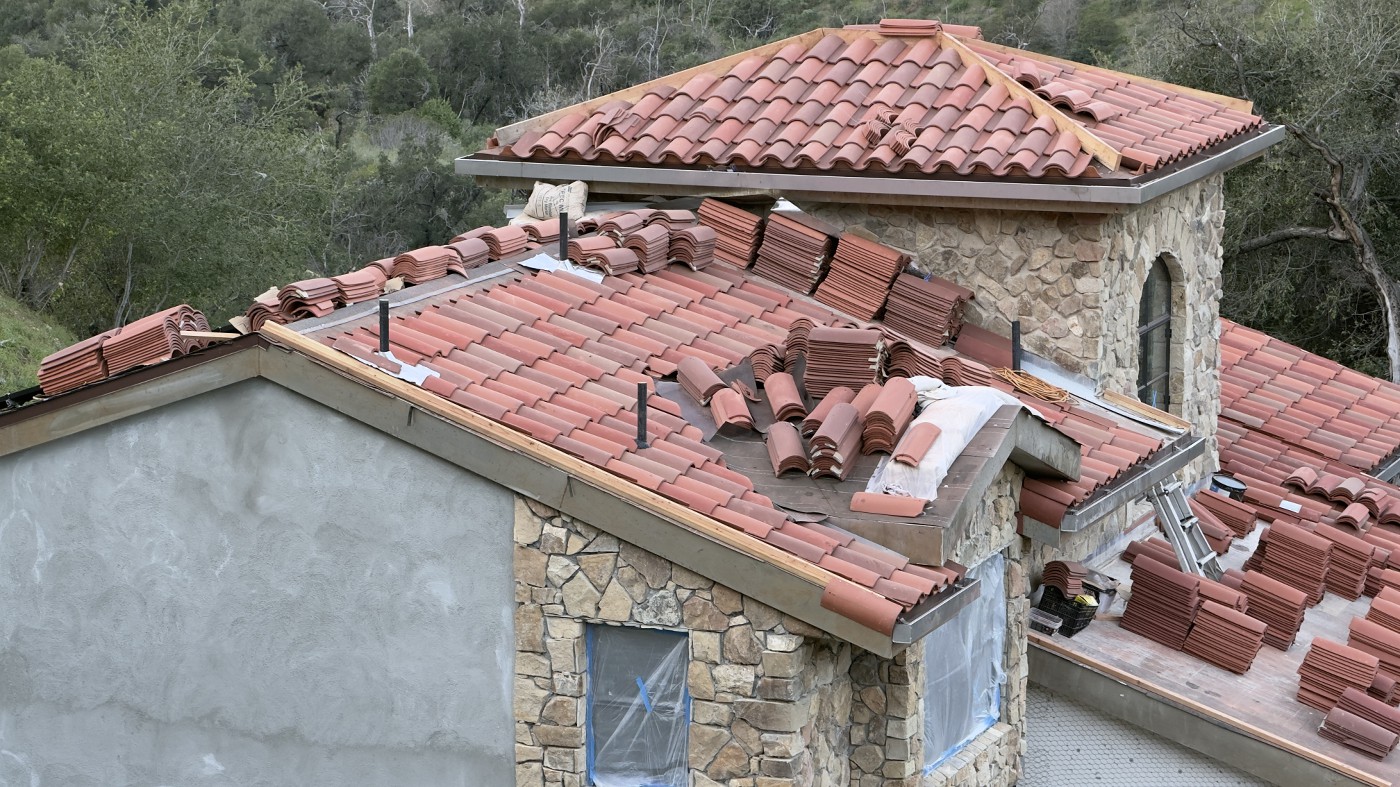 artly tiled terracotta roof on a stone and plaster building, with stacks of extra tiles and plastic over the window openings.