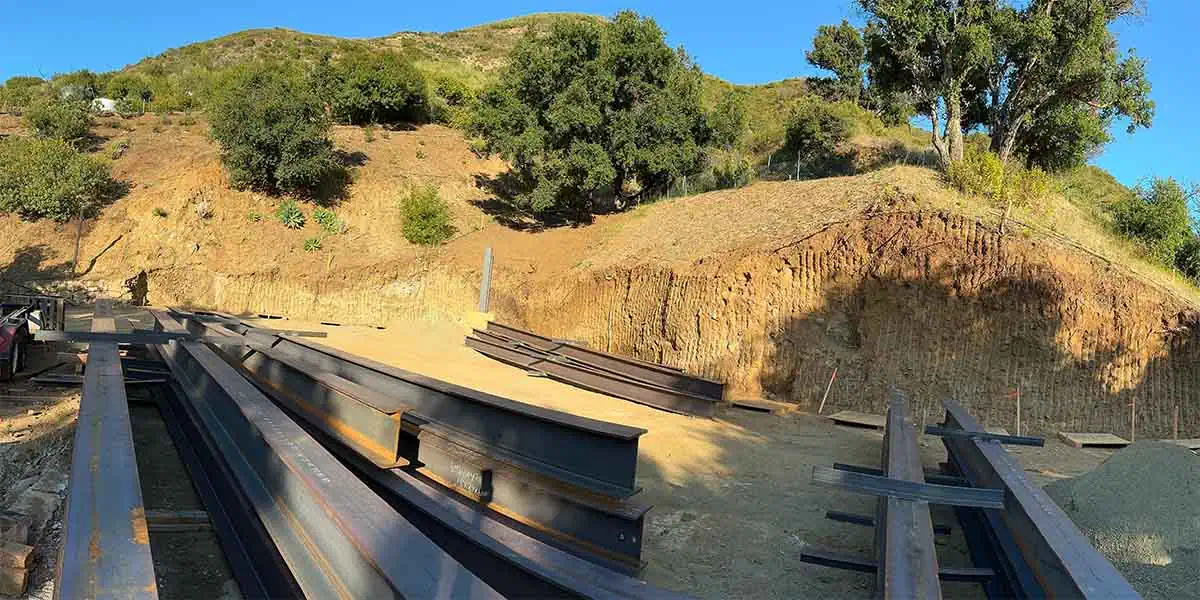 Steel beams laid out beside a graded building pad