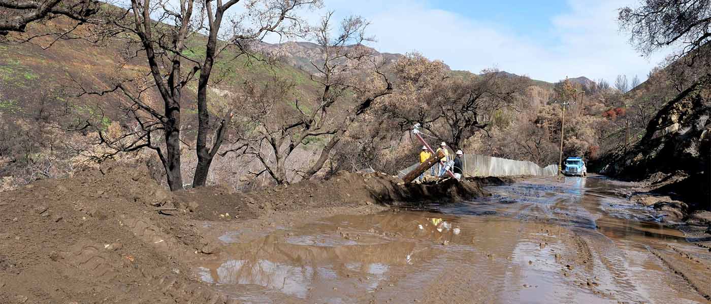 Crew working on a mud-covered canyon road with a downed pole