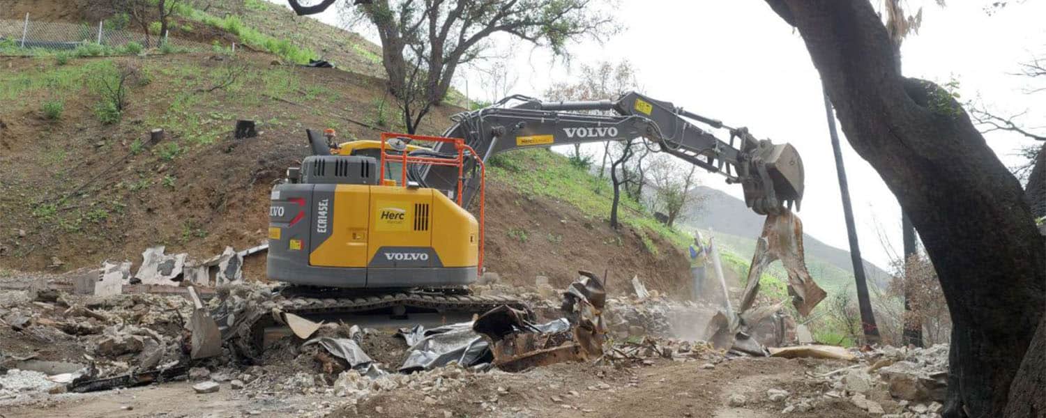 Excavator clearing burned debris near a burned tree