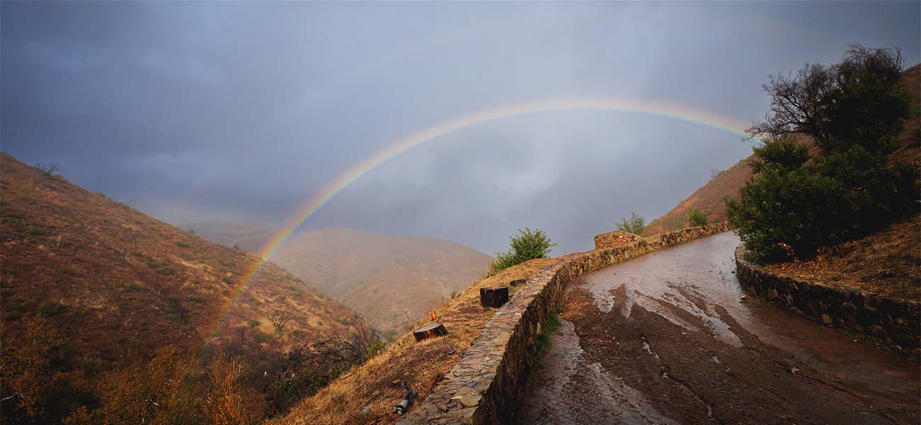 Rainbow over a canyon road running with rainwater